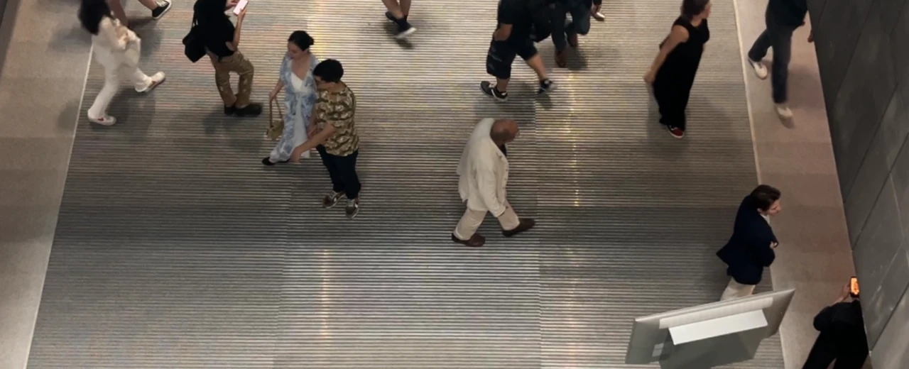Vogelperspektive auf Menschen, die auf einem Metallboden gehen.  Gedämpfte Farben, geriffelter Boden, elektronisches Display.