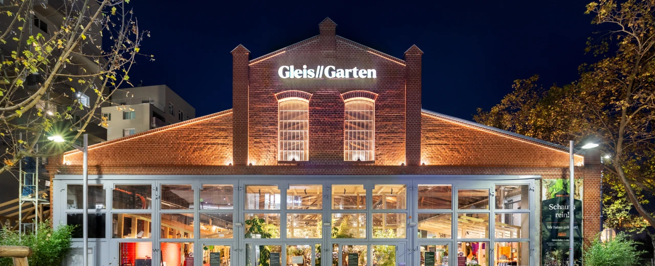 © Gleis//Garten Gleis/Garten in Berlin bei Nacht. Rotziegelgebäude mit beleuchtetem Namensschild und großen Fenstern.