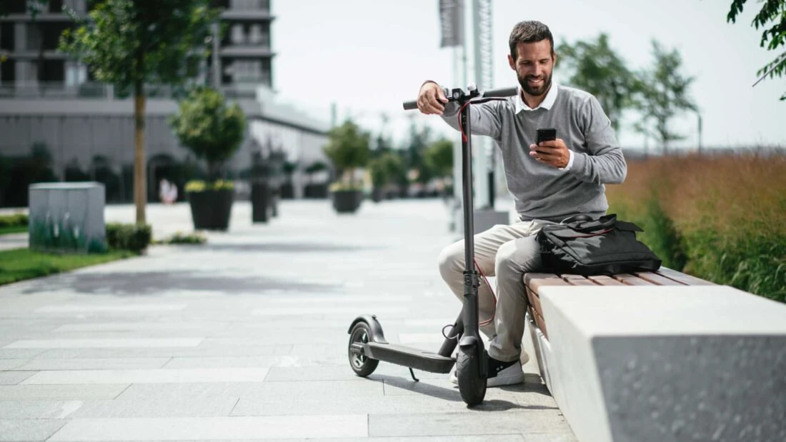 Mann mit Roller sitzt auf Bank vor einem Wohn-Investment