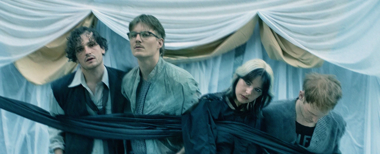 Bandfoto: Vier Musiker, verbunden durch Stoff, vor einem Hintergrund aus lichtdurchlässigen Stoffen. Stilvolles, geheimnisvolles Bild.