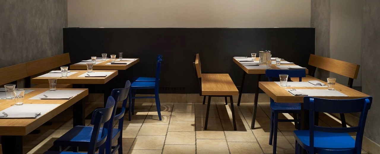 © Pizza Posto, Nilo Klotz Moderner Restaurantbereich mit hellen Holztischen & dunkelblauen Stühlen. Minimalistisches Design.