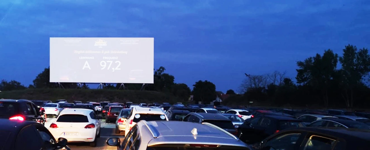 Autokino bei Nacht mit vielen Autos vor einer großen Leinwand, auf der ein Messwert angezeigt wird.