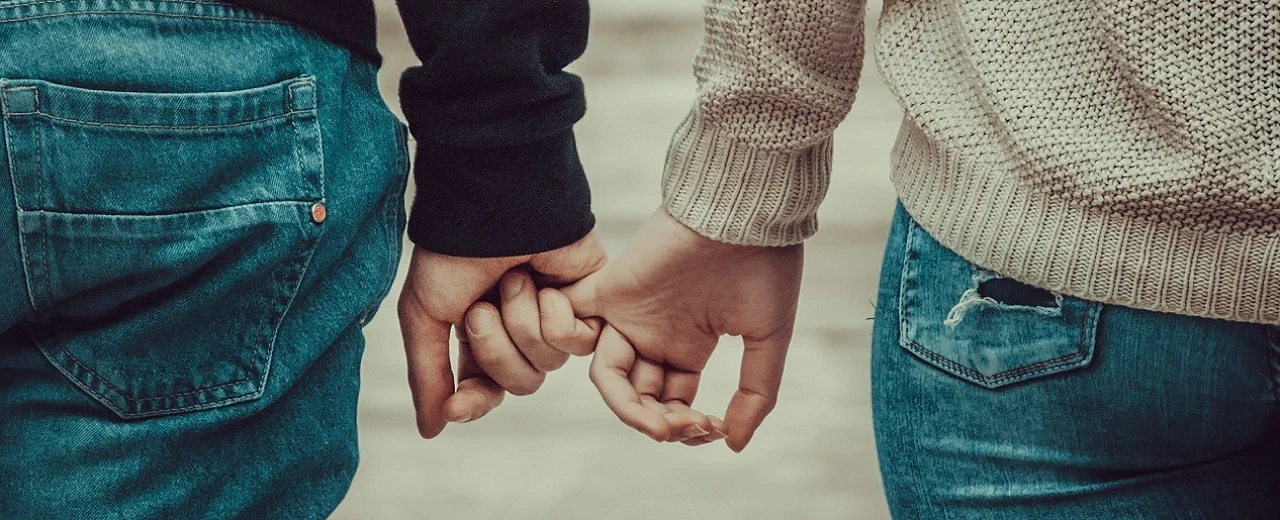 Nahaufnahme zweier Personen, die sich an den Händen halten. Nur Rücken und Hände sichtbar. Jeans und Pullover.