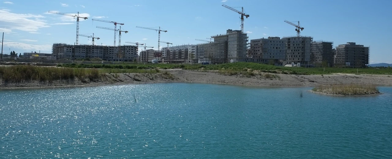 Hochhausbau am See: Mehrere Gebäude im Bau mit vielen Baukränen.