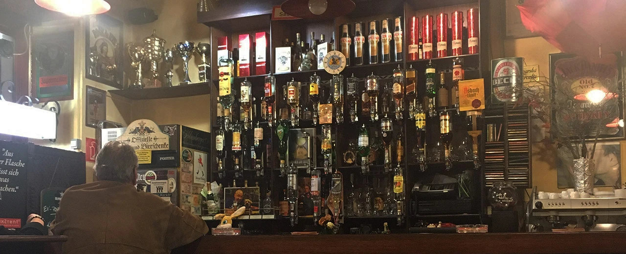 Gemütliche Kneipentheke mit vielen Flaschen, Bildern und einem Gast. Angenehme Atmosphäre.