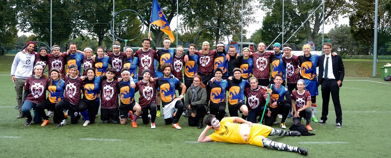Gruppenfoto eines Quidditch-Teams in einheitlichen Trikots mit Wolfs- und Pferde-Motiven auf dem Spielfeld.