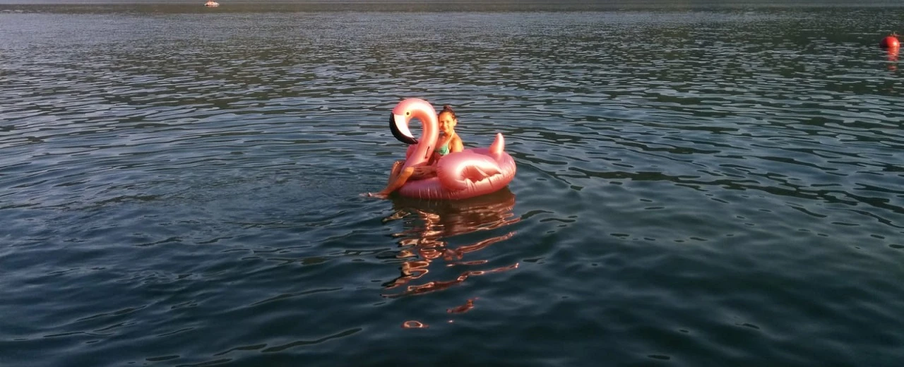 © Miriam Kummer Mädchen auf rosa Flamingo Schwimmtier im See.