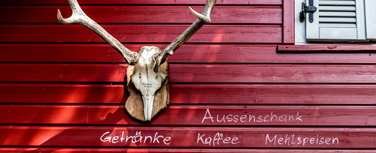 Hirschgeweih an roter Holzwand mit Kreidebeschriftung: Aussenschank, Getränke, Kaffee, Mehlspeisen.