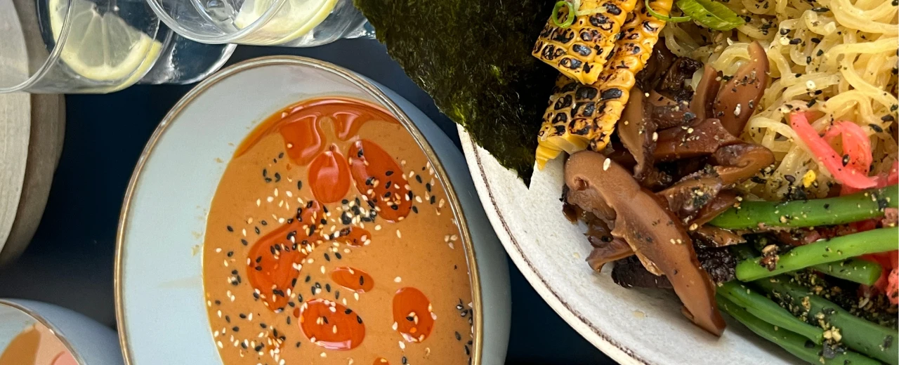 Appetitliches Bild von Ramen mit verschiedenen Toppings und einer separaten Sesam-Sauce. Canva.