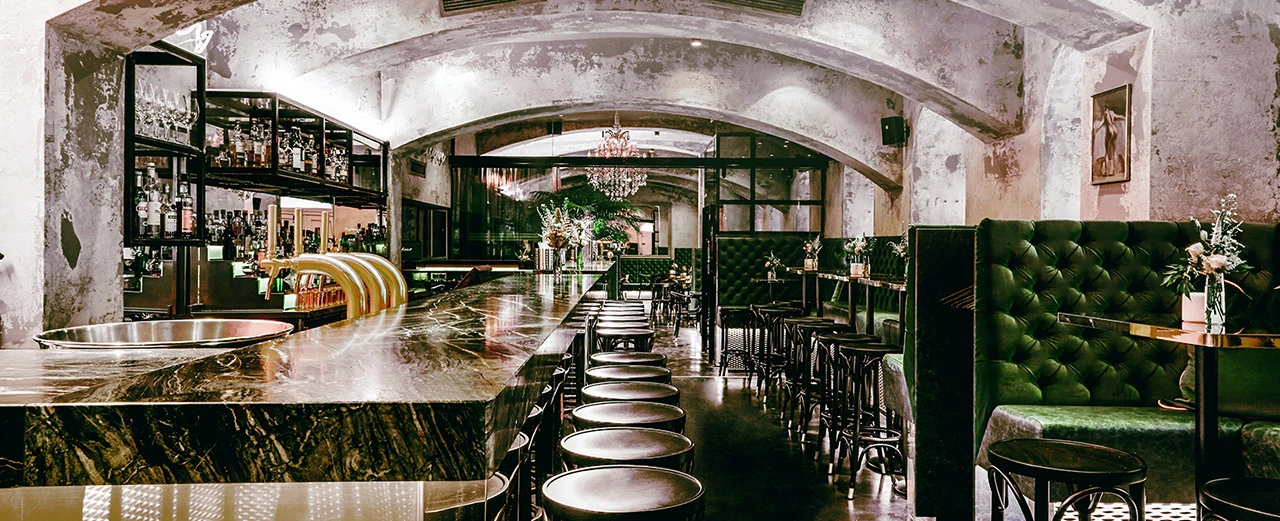 © Motto Stilvolle Bar mit Marmor-Theke, dunklen Holzstühlen & grüner Samtbank. Gewölbte Decke & indirekte Beleuchtung.