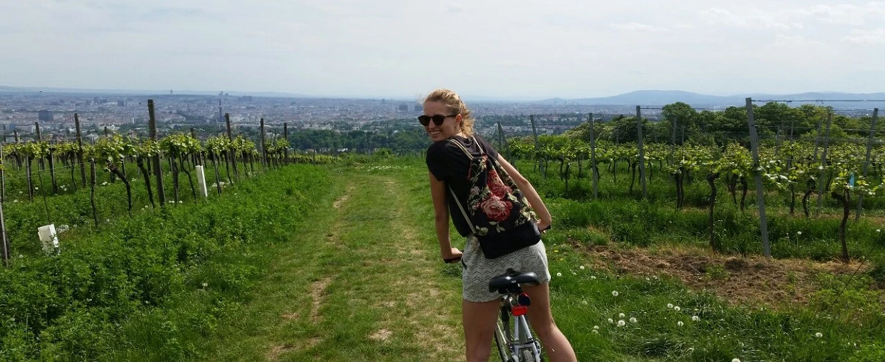 © Alina Lindermuth Frau fährt Fahrrad durch Wiener Weinberge, Panoramablick auf Wien.