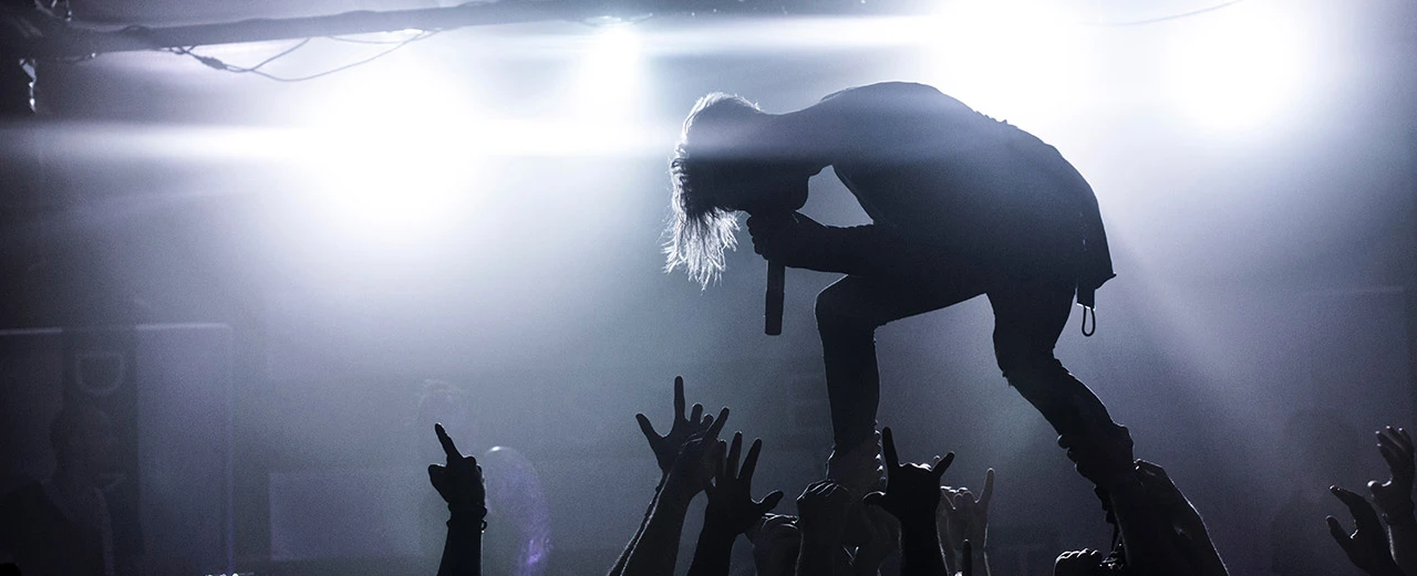 Silhouette eines Sängers, der auf den Händen des Publikums steht und während eines Konzerts singt. Bühnenlicht und Rauch.