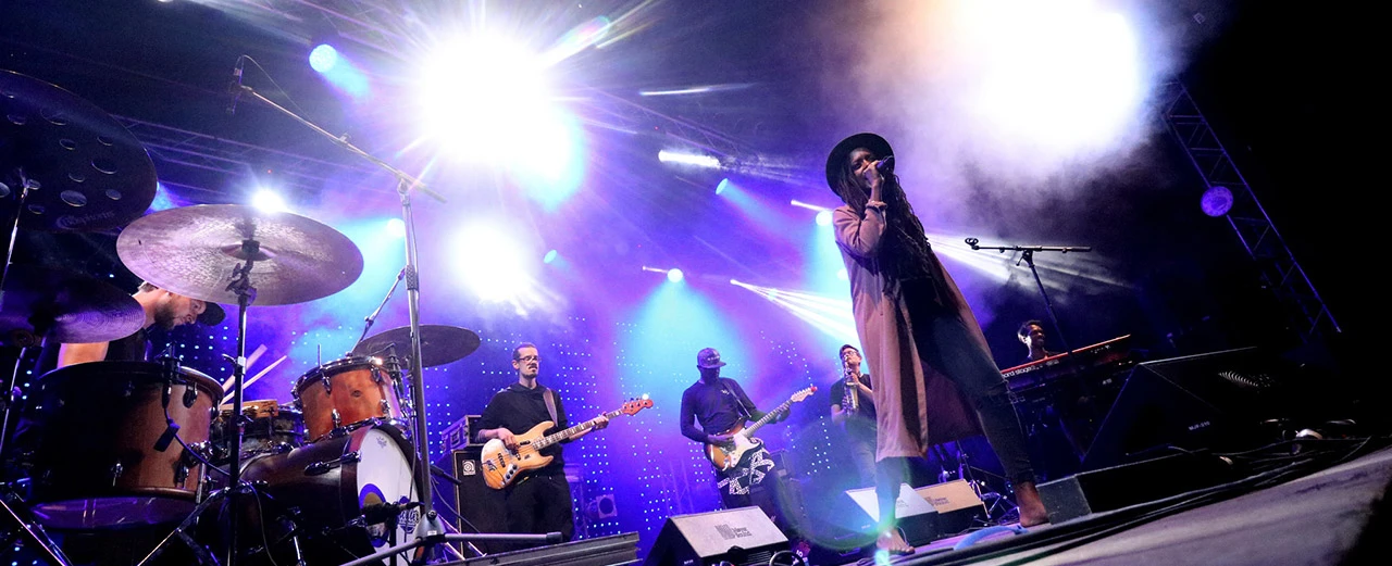 Live-Band-Performance auf der Bühne mit Scheinwerfern. Sängerin im Vordergrund, Musiker mit Gitarren und Schlagzeug im Hintergrund.