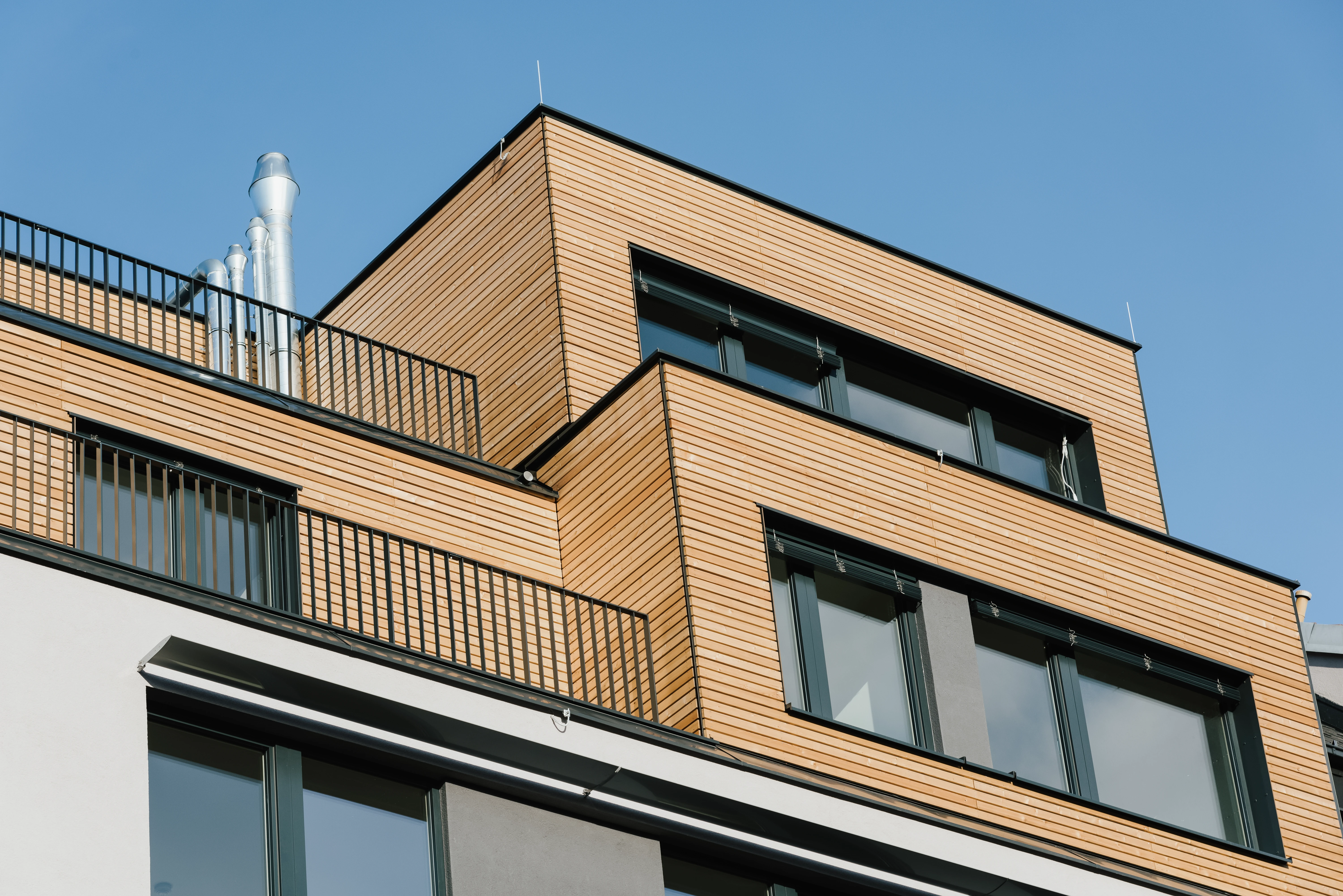 Wohninvestment mit Holzfassade und Balkone mit schwarzem Metall