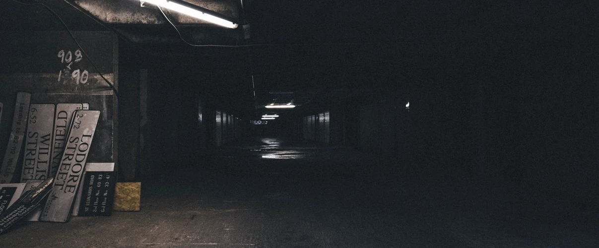 Dunkler Gang mit alten Straßenschildern und schwacher Beleuchtung. Düsteres, verlassenes Ambiente.