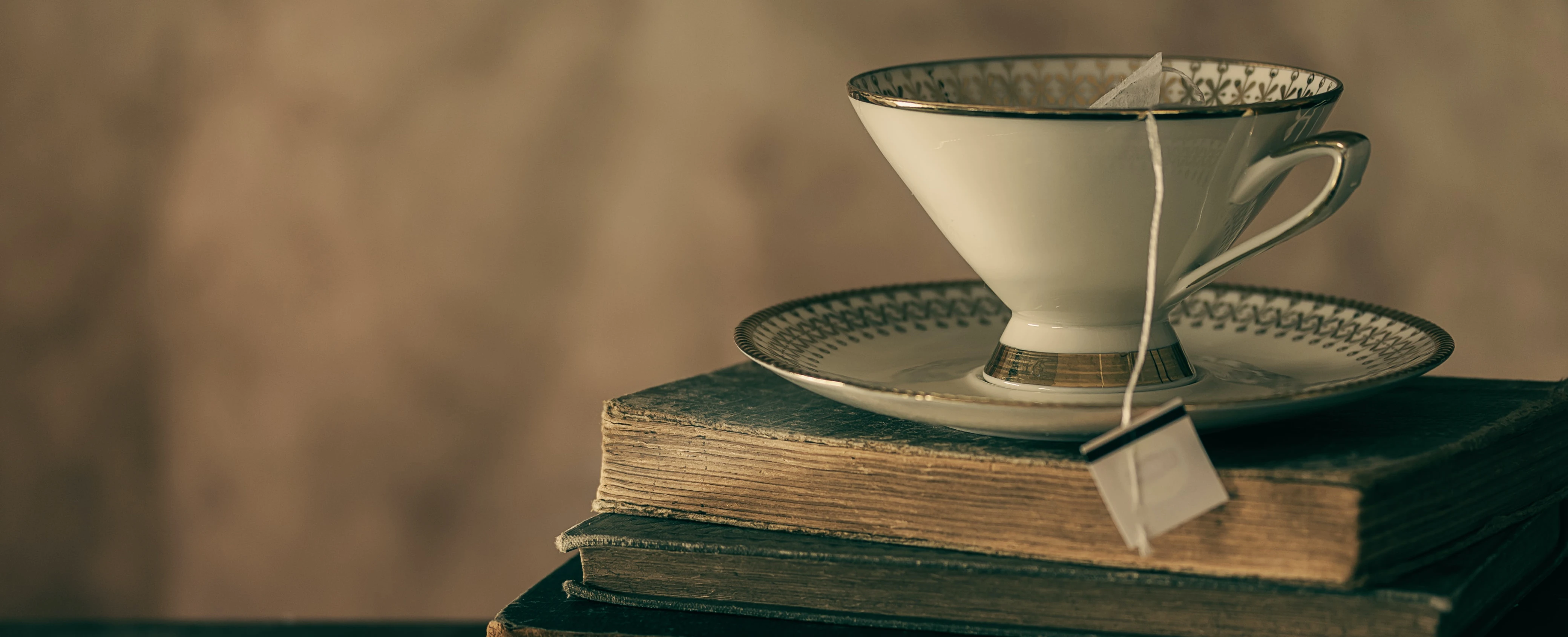 Eine weiße Teetasse mit goldenen Verzierungen auf alten Büchern.  Nostalgisches Bild.