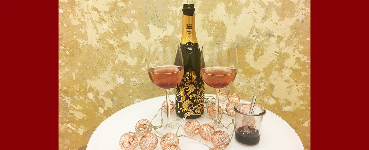 Zwei Gläser Roséwein und eine Flasche Katiús Rosé Sekt auf einem Tisch mit roségoldenen Lichtern. Perfekt für besondere Anlässe.