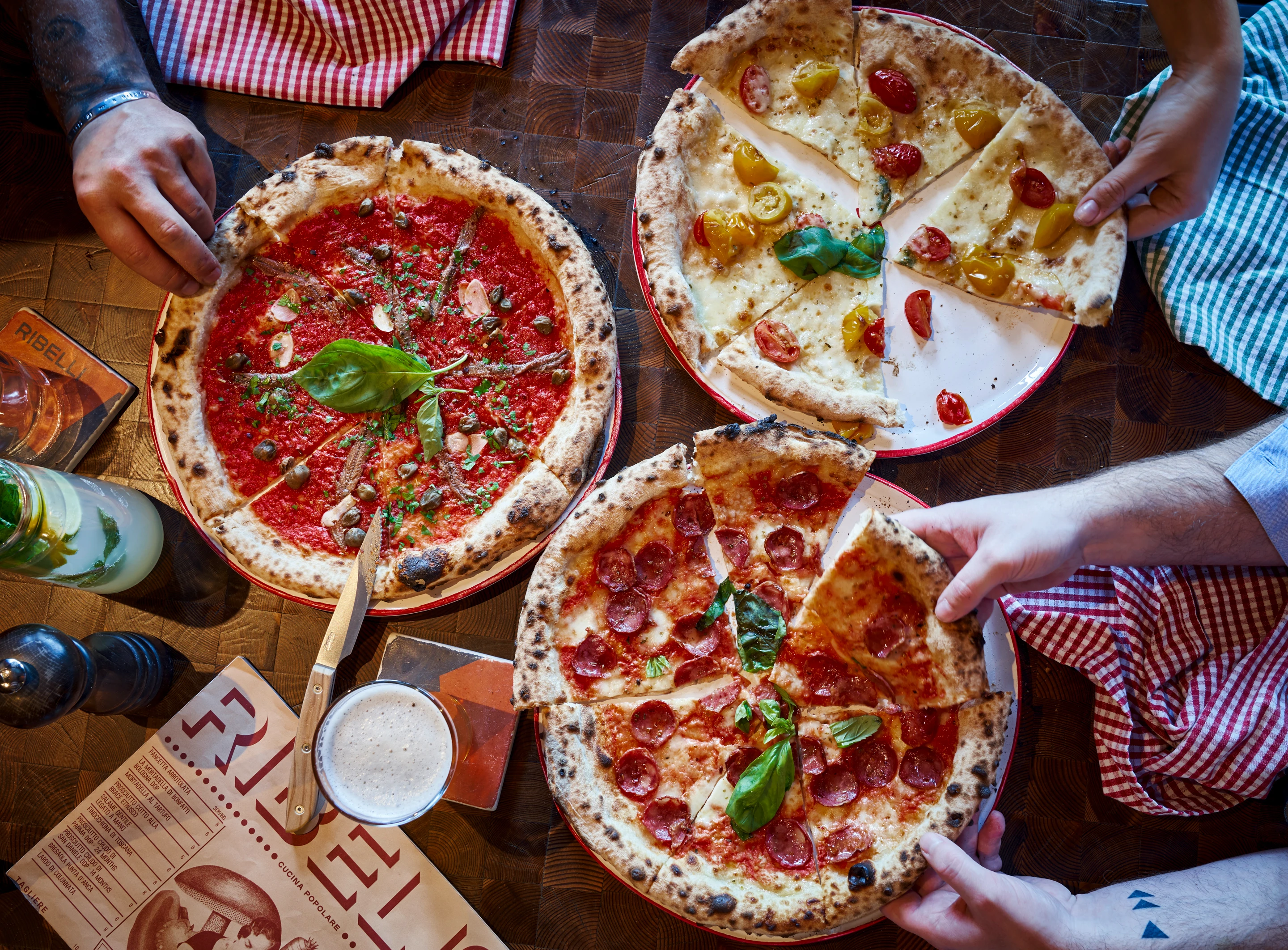 Drei verschiedene Pizzen werden von mehreren Personen geteilt. Leckere italienische Küche in gemütlicher Atmosphäre.