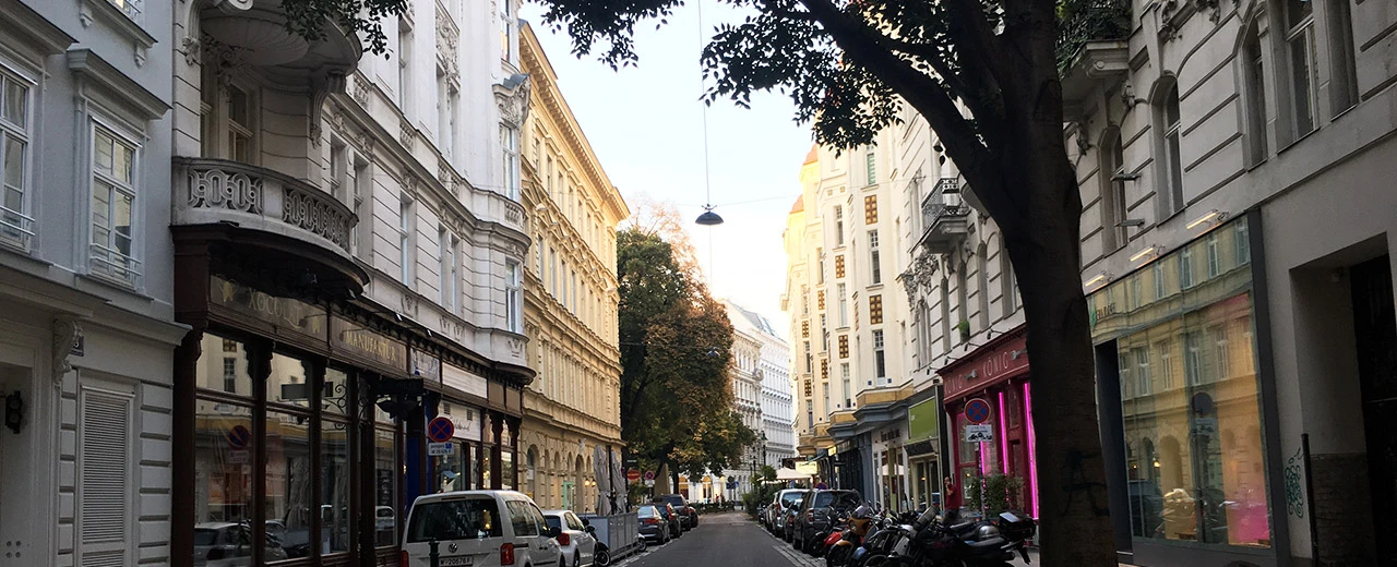 Ruhige Wiener Straße mit historischen Gebäuden, Bäumen und parkenden Autos.
