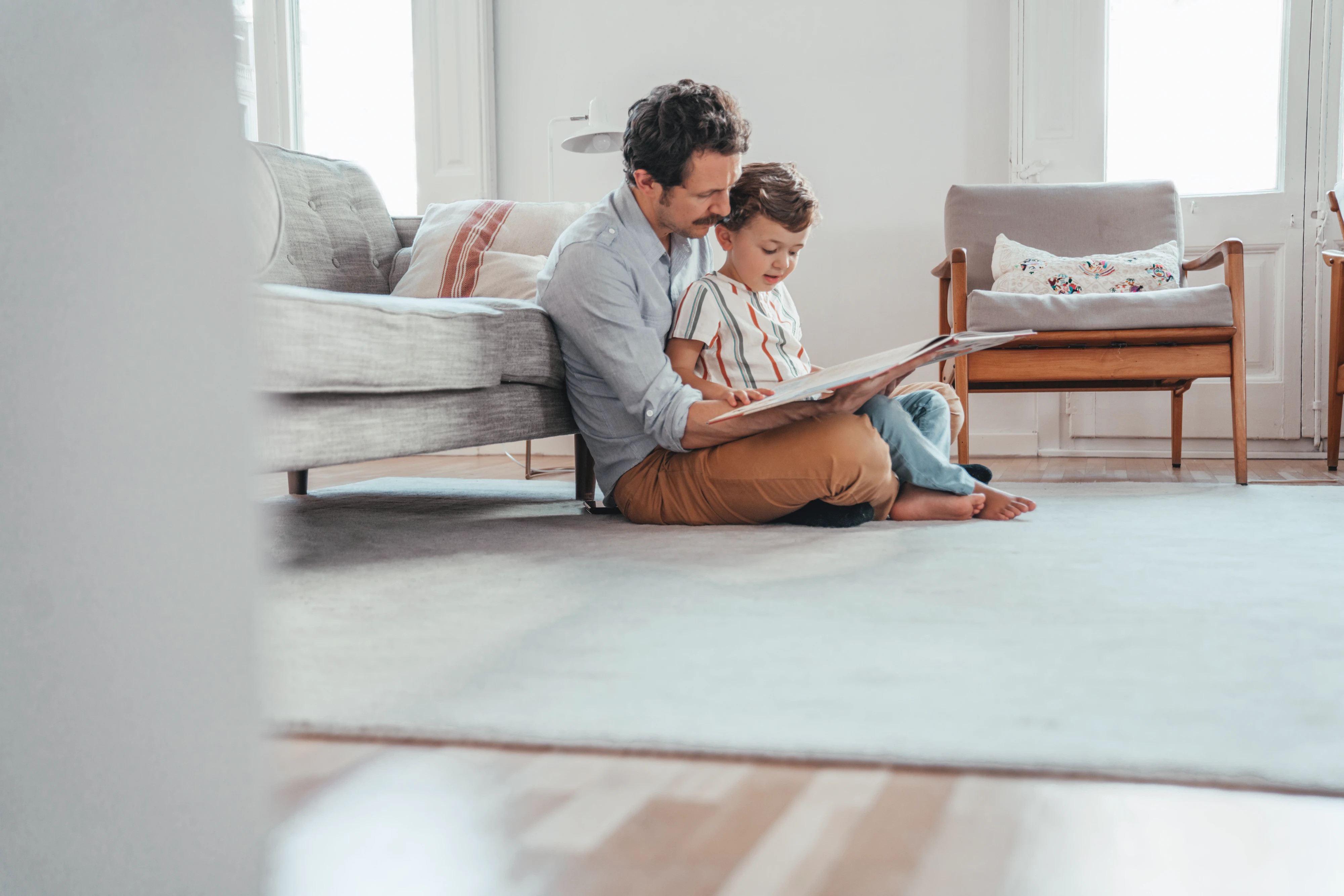 Vater und Kleinkind sitzen am Boden und lesen ein Buch in Wohnzimmer