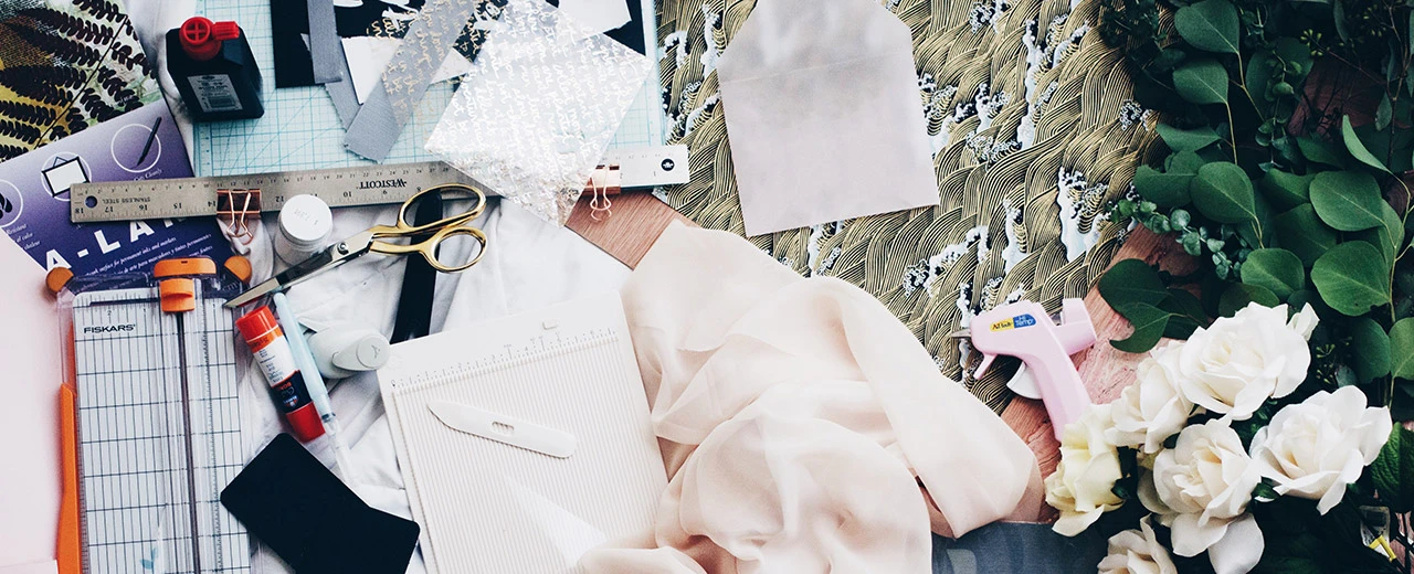 Bastelutensilien wie Scheren, Lineale, Papier, Stoff & Blumen auf einer Arbeitsfläche. DIY, Scrapbooking, Kartenbasteln.