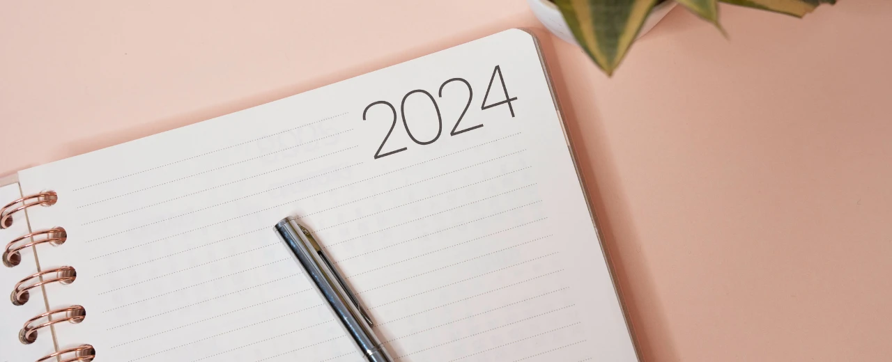 Notizbuch mit der Jahreszahl 2024, Stift und rosafarbenem Hintergrund.