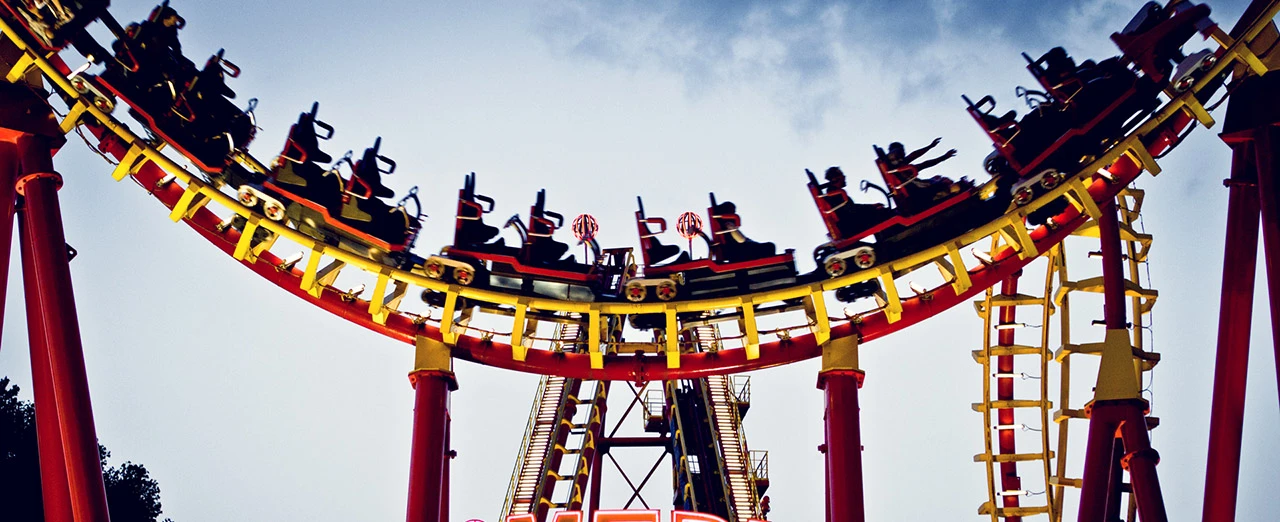 Achterbahnfahrt in einem Vergnügungspark. Rote und gelbe Wagen fahren eine Kurve.