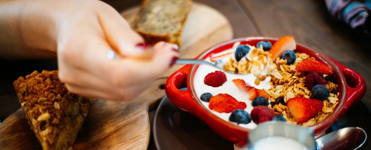 Frau isst gesundes Frühstück: Joghurt mit Granola und Beeren in roter Schale.