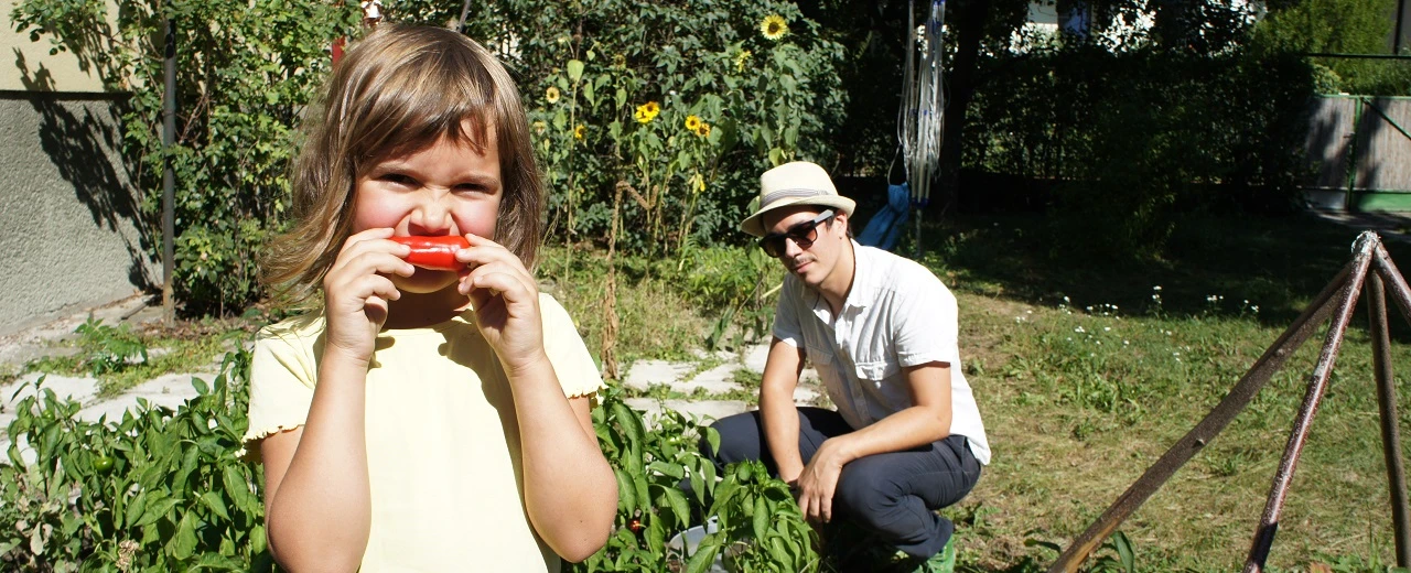 © Miriam Kummer Mädchen isst Paprika im Garten, Mann daneben.