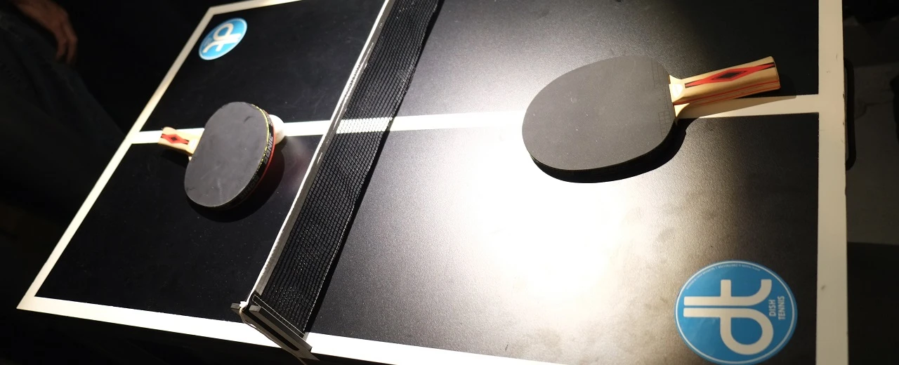 Zwei Tischtennisschläger auf einer schwarzen Tischtennisplatte mit Netz.