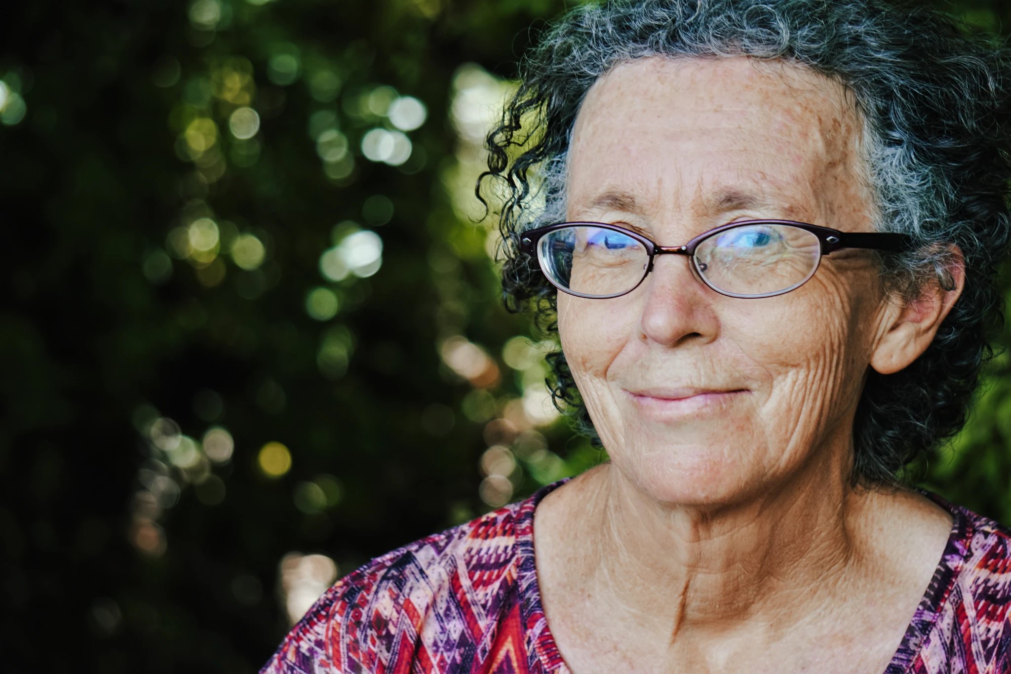 Ältere Dame mit Brille und Locken lächelt in Kamera