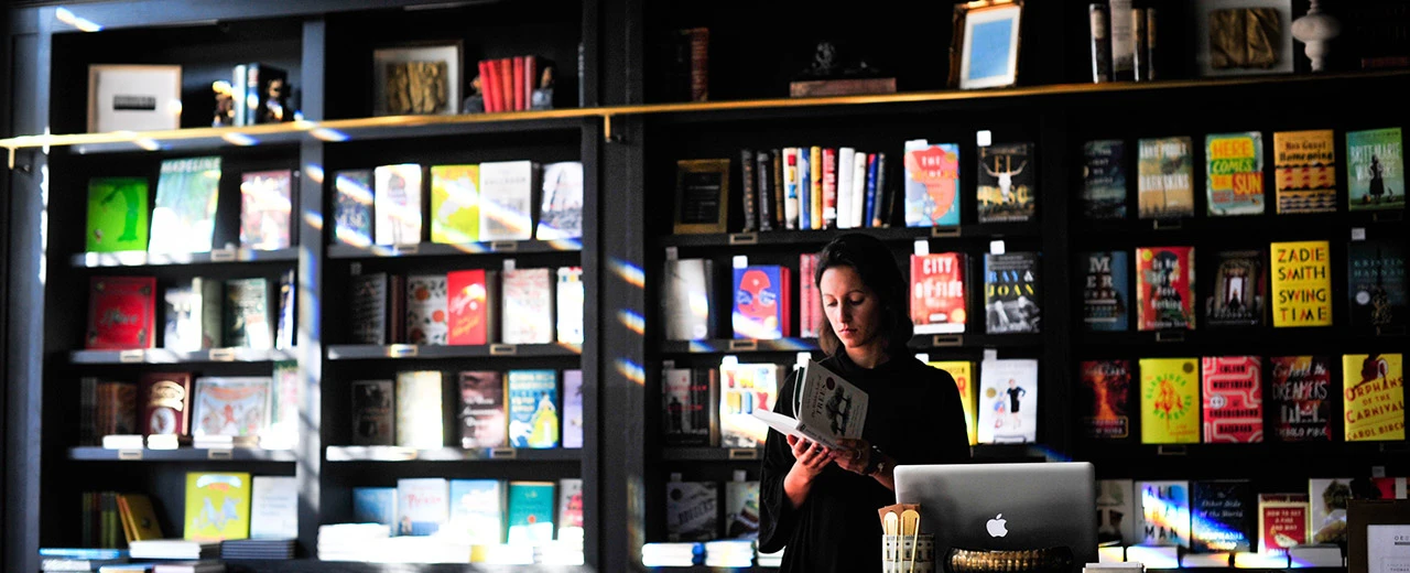 © Photo by Pj Accetturo on Unsplash Junge Frau liest in einer gut sortierten Buchhandlung mit vielen Büchern in den Regalen.  Bild bearbeitet mit Adobe Photoshop.