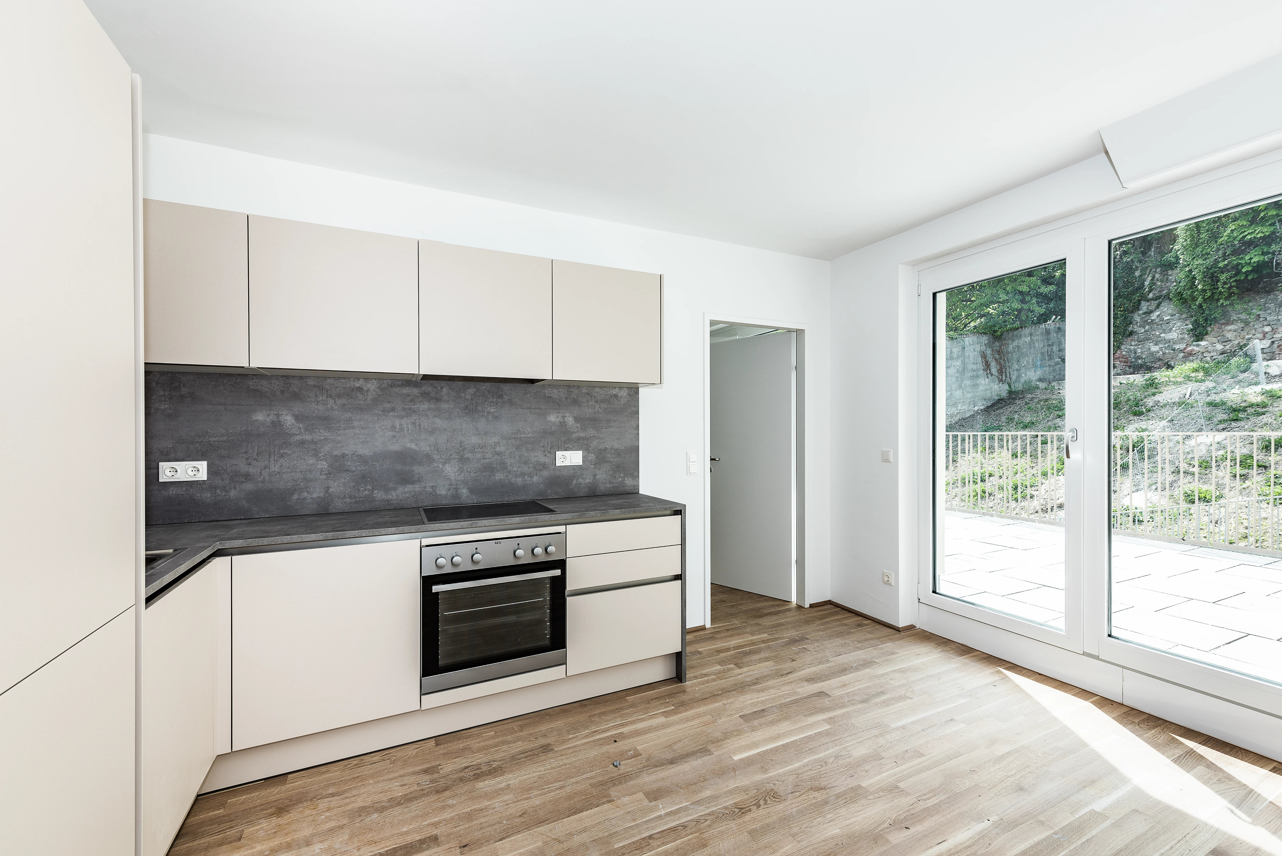 Moderne Küche mit heller Verkleidung und dunkelgrauen Arbeitsplatten und Blick auf Terrasse