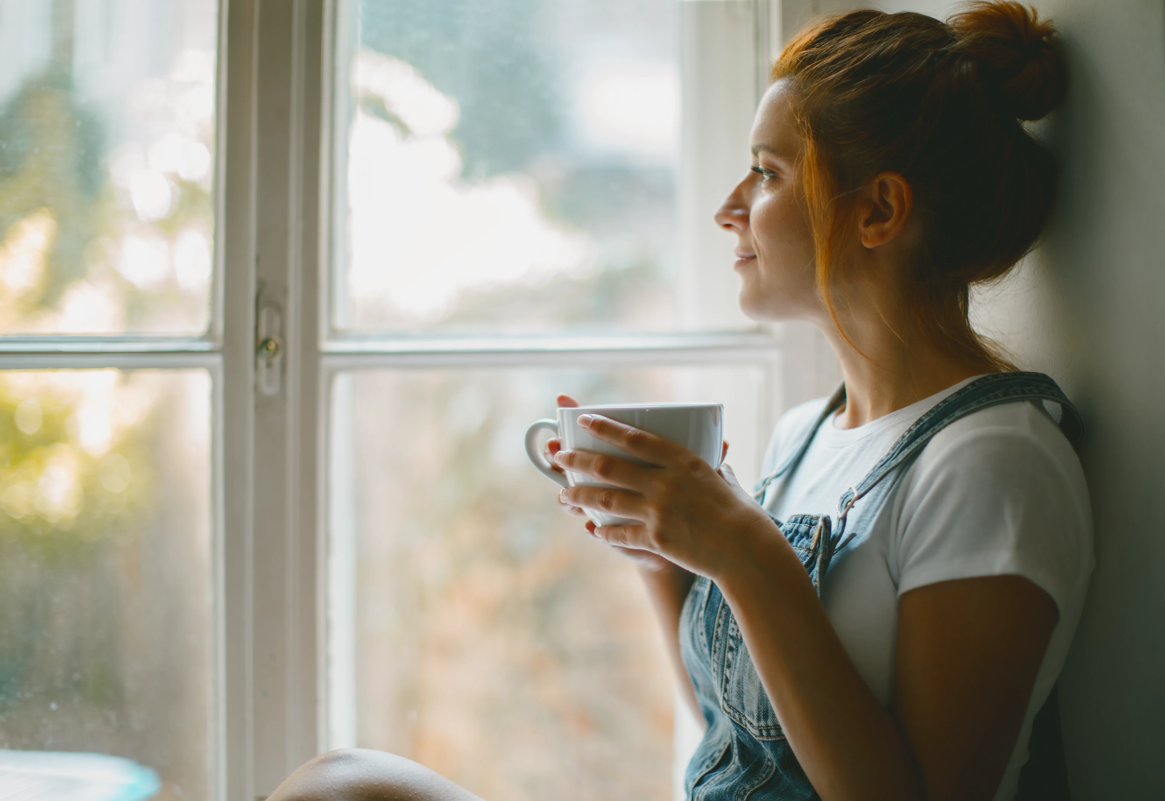 Junge Frau blickt mit Kaffeetasse aus Altbau Fenster
