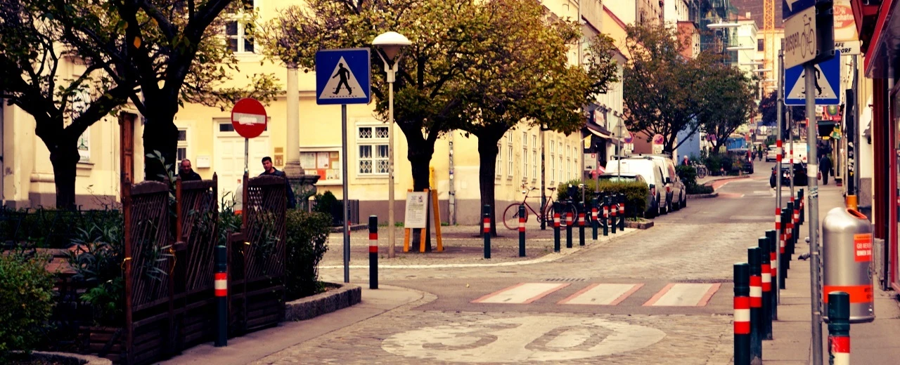 Ruhige europäische Straße mit Fußgängerüberweg, Bäumen & Fahrrädern. Verkehrszeichen sind sichtbar.