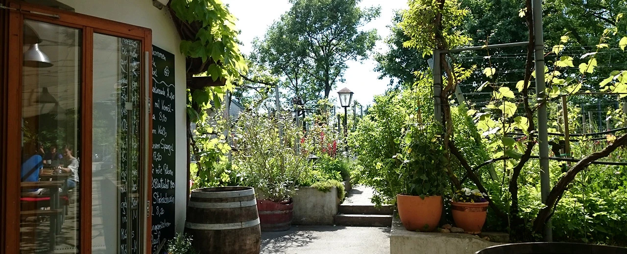 © Miriam Kummer Gemütlicher Restaurant-Außenbereich mit blühenden Pflanzen und Weinfässern.