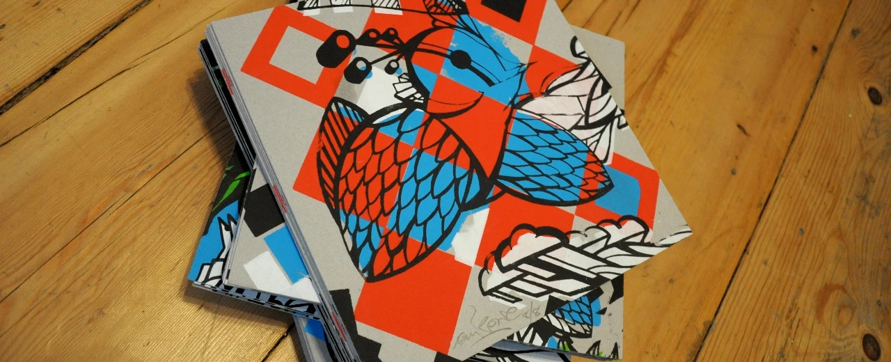 Stapel grafischer Kunstdrucke in Rot, Blau, Weiß & Schwarz auf Holz.