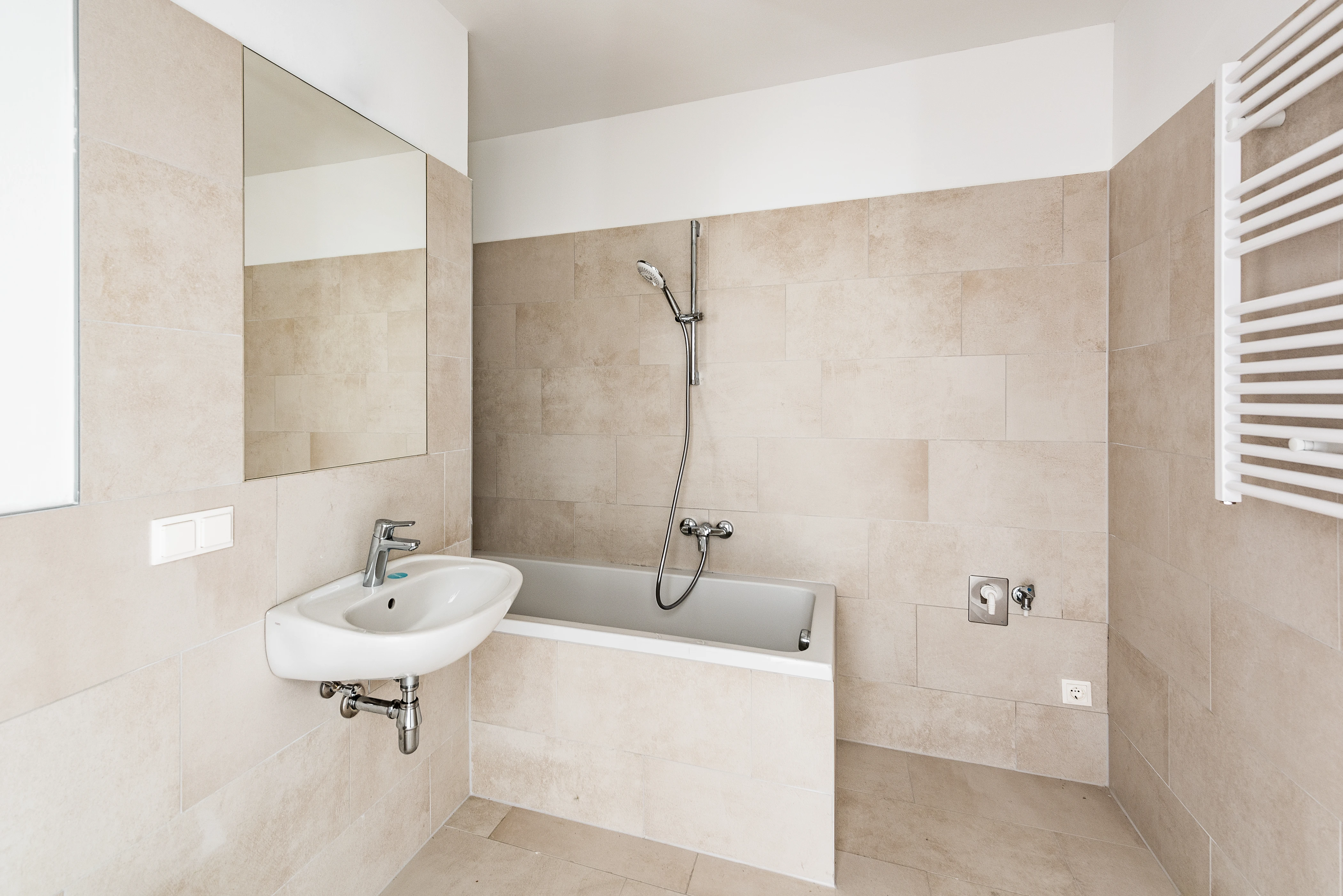 Badezimmer mit Badewanne und hellbeigen Fliesen