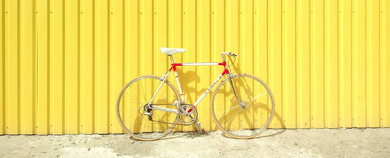 Weiß-rotes Rennrad vor gelber Metallwand. Fahrradfahren, Retro-Design, Vintage.