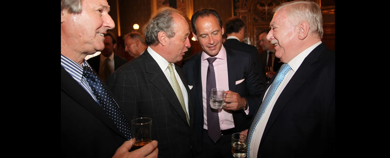 Bild einer Gruppe von Männern in Anzügen, die sich auf einer Veranstaltung unterhalten.