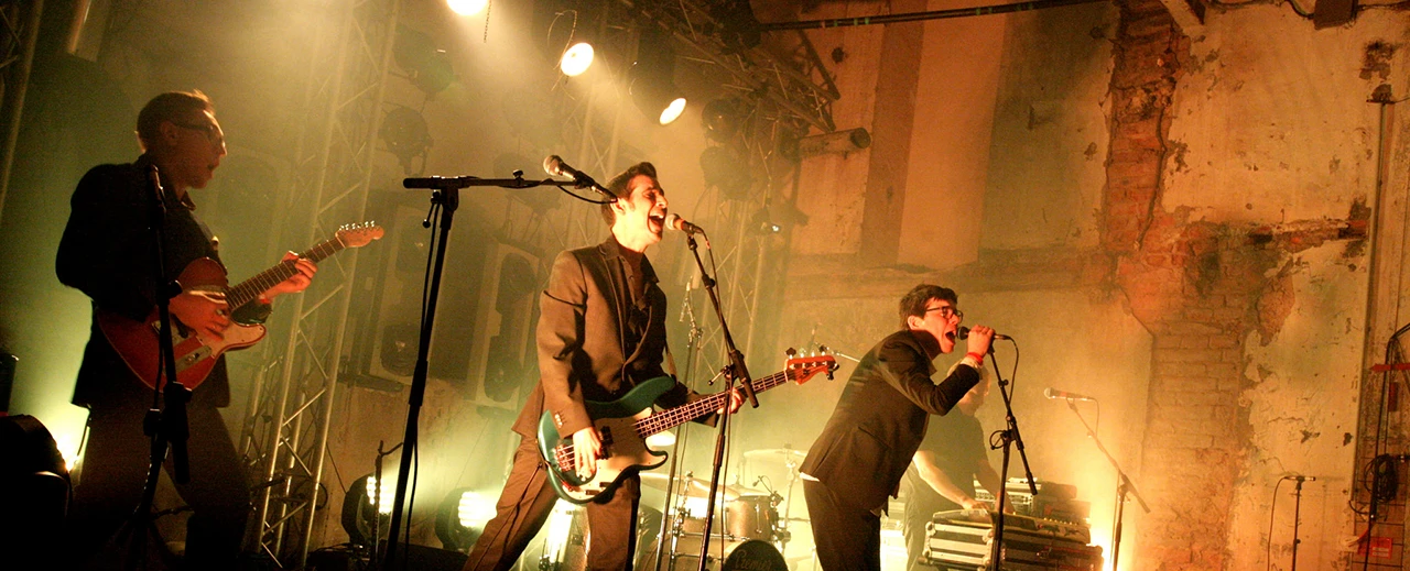 Eine Band gibt eine energiegeladene Live-Performance auf einer abgenutzten, aber stimmungsvollen Bühne.