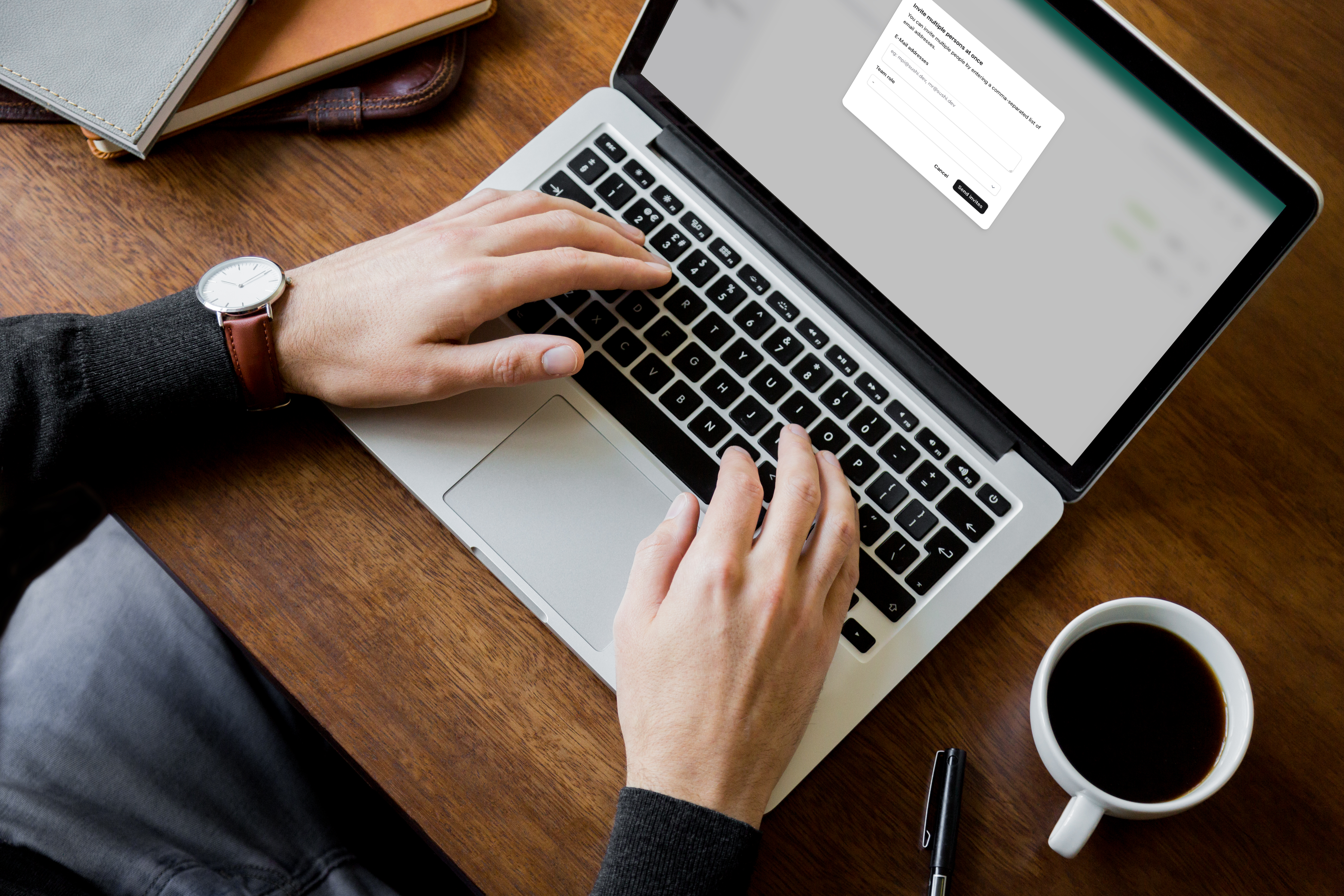 Overhead view of a person typing on a laptop on a wooden desk with a coffee mug and notebooks nearby.