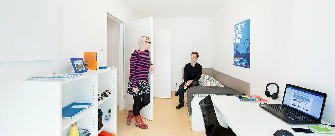 Moderner Studentenwohnraum: Zwei Studenten in einem hellen Zimmer mit Bett, Schreibtisch & Laptop. Foto von Barbara Mair.