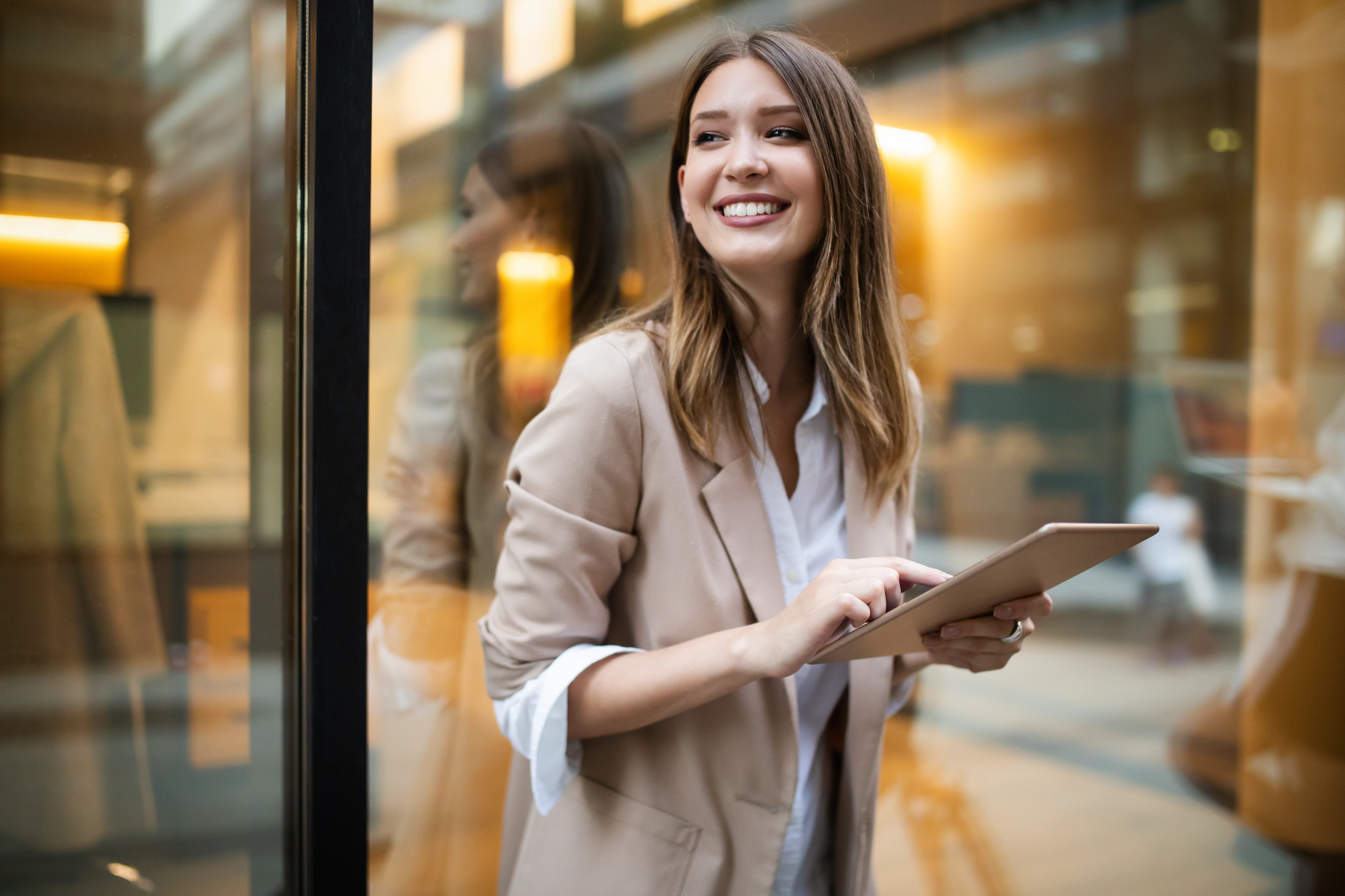 Lachende Frau mit Tablet vor Fensterfassade