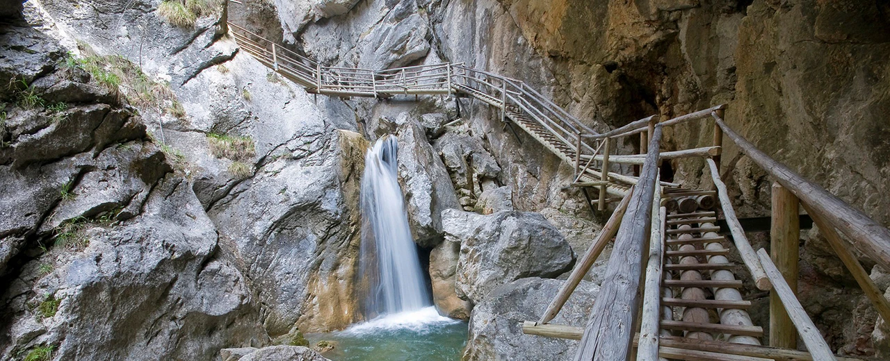 © Bärenschutzklamm Panoramablick auf einen Wasserfall in einer Schlucht mit Holzstegen und Treppen als Wanderweg.