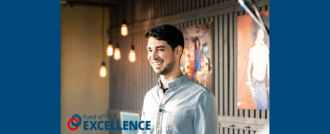 © Fund of Excellence Lächelnder Mann im Hemd vor Kunstwerken und Edison-Glühbirnen. Fund of Excellence Kampagne.