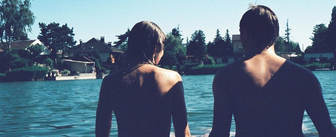 © Miriam Kummer Zwei Personen stehen im See, Blick auf Häuser und Bäume. Sommerlicher Tag.