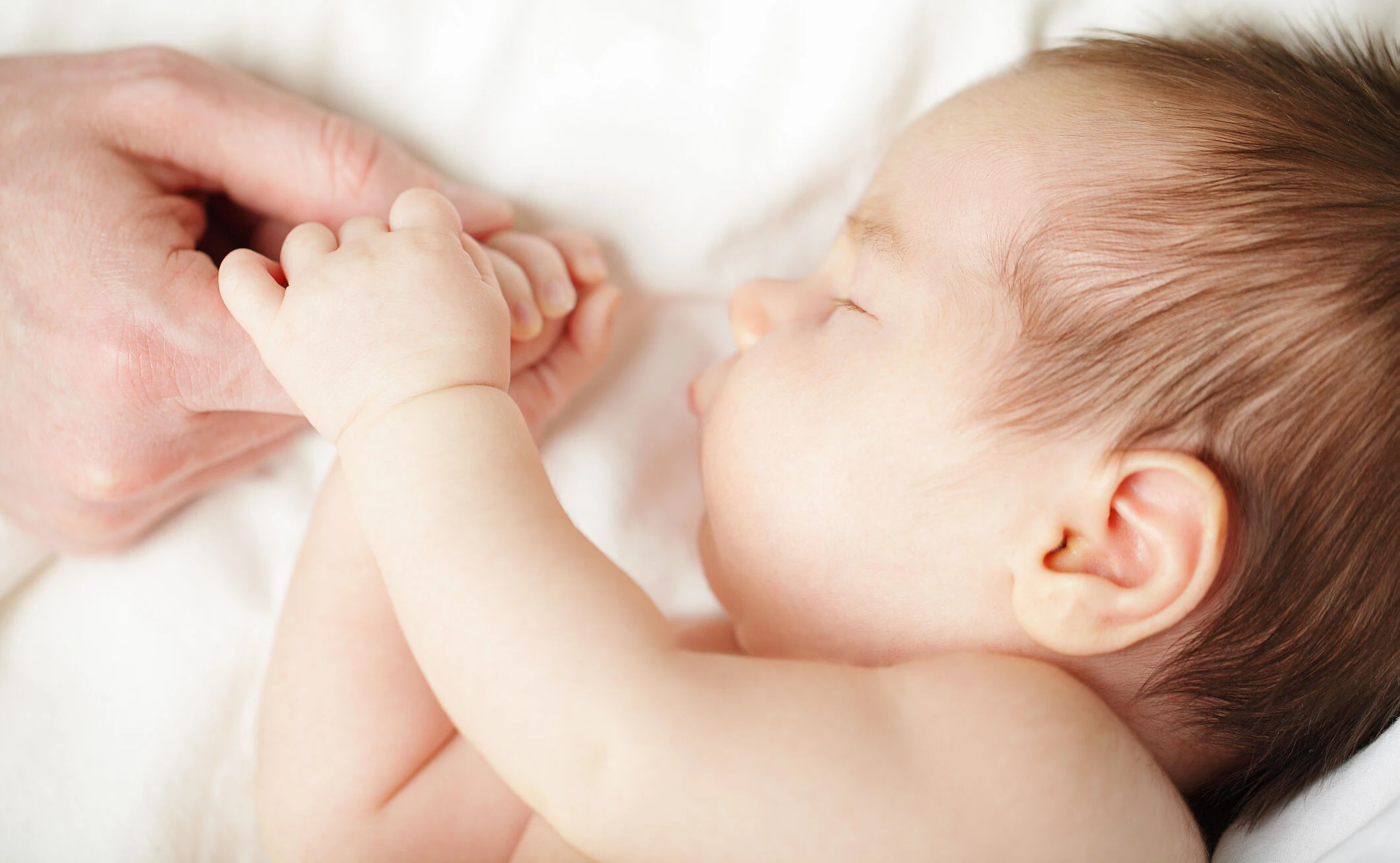 Baby, das schläft und dabei die Hand seiner Mutter hält