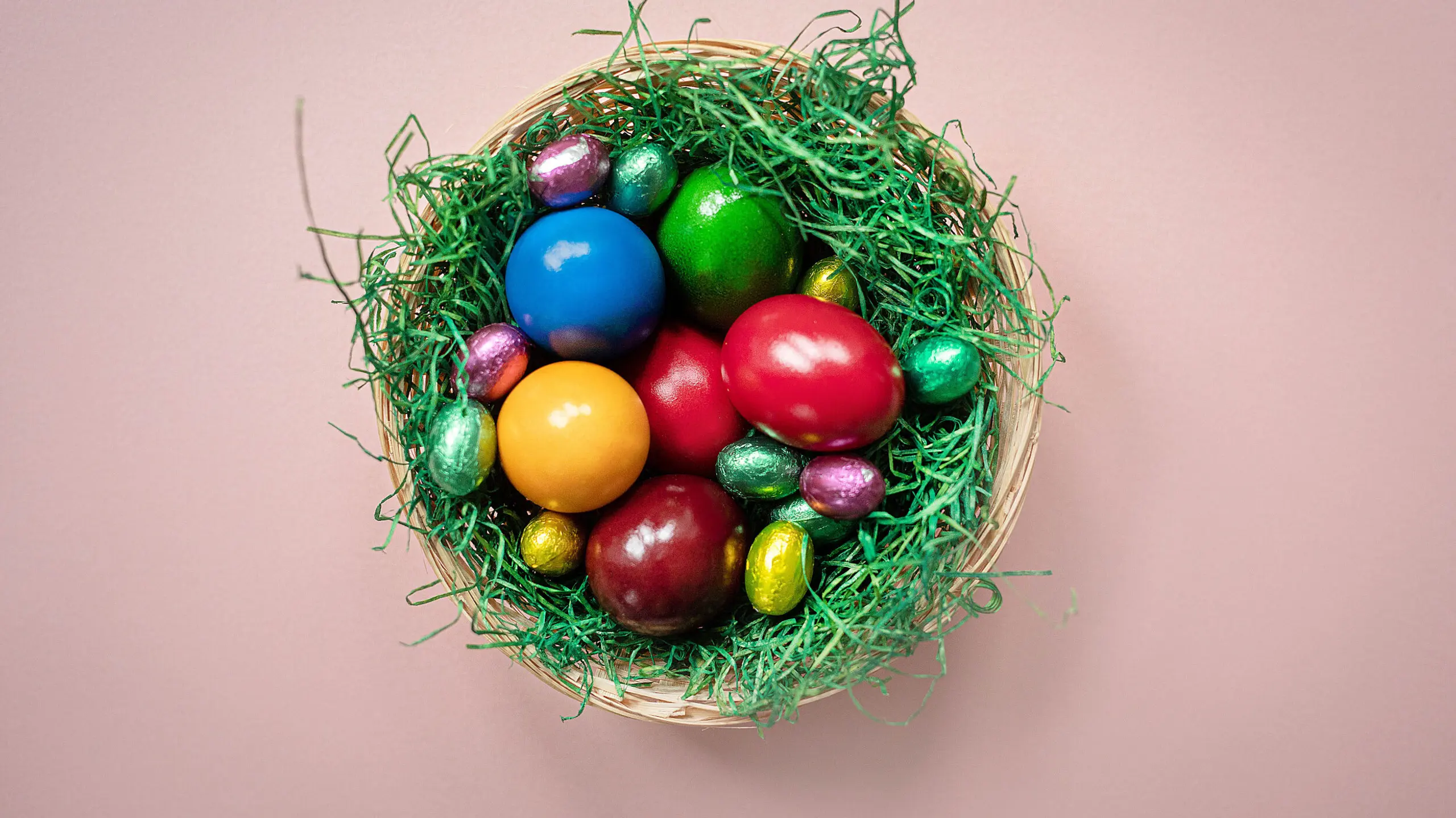 Osternest mit bunten Ostereiern, das auf einem rosa Hintergrund steht