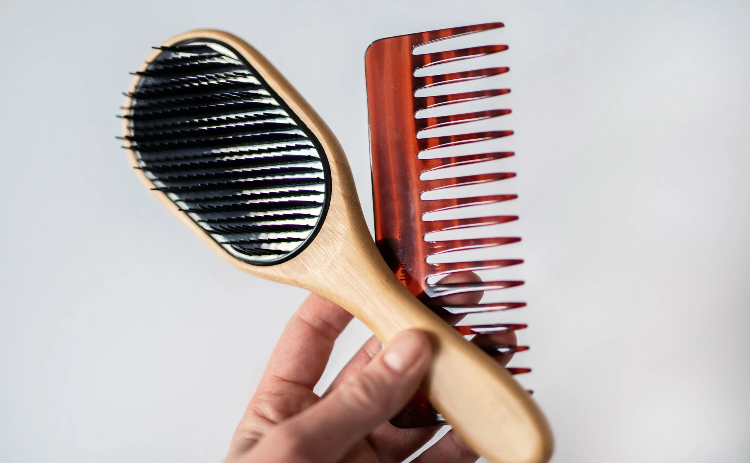 Frauenhand, die eine Haarbürste und einen Haarkamm hält